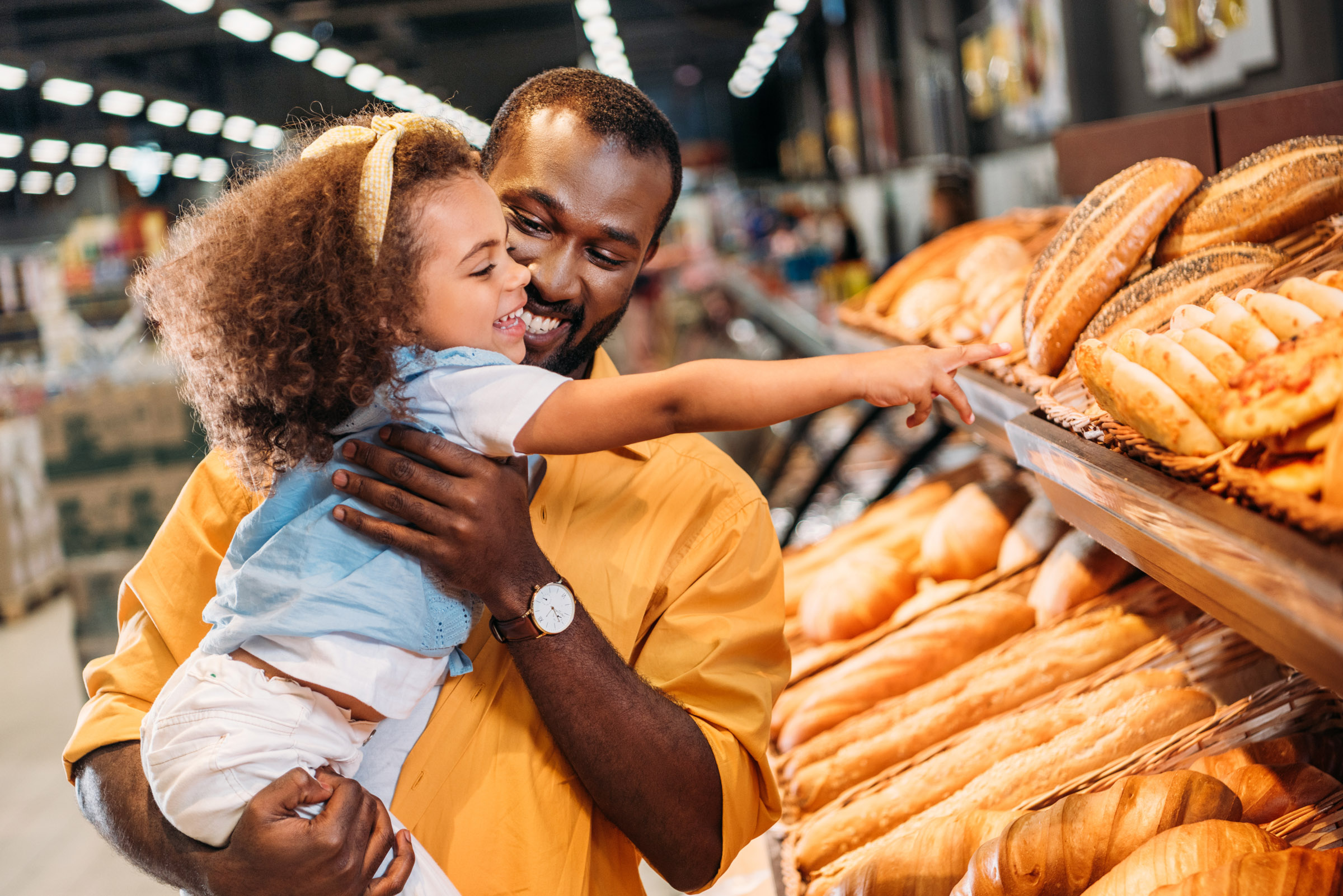 father carrying daughter pointing at bakery bread
