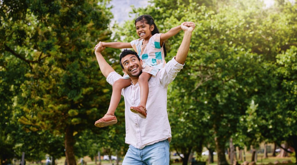 father lifting daughter onto shoulders in park father lifting daughter onto shoulders in park