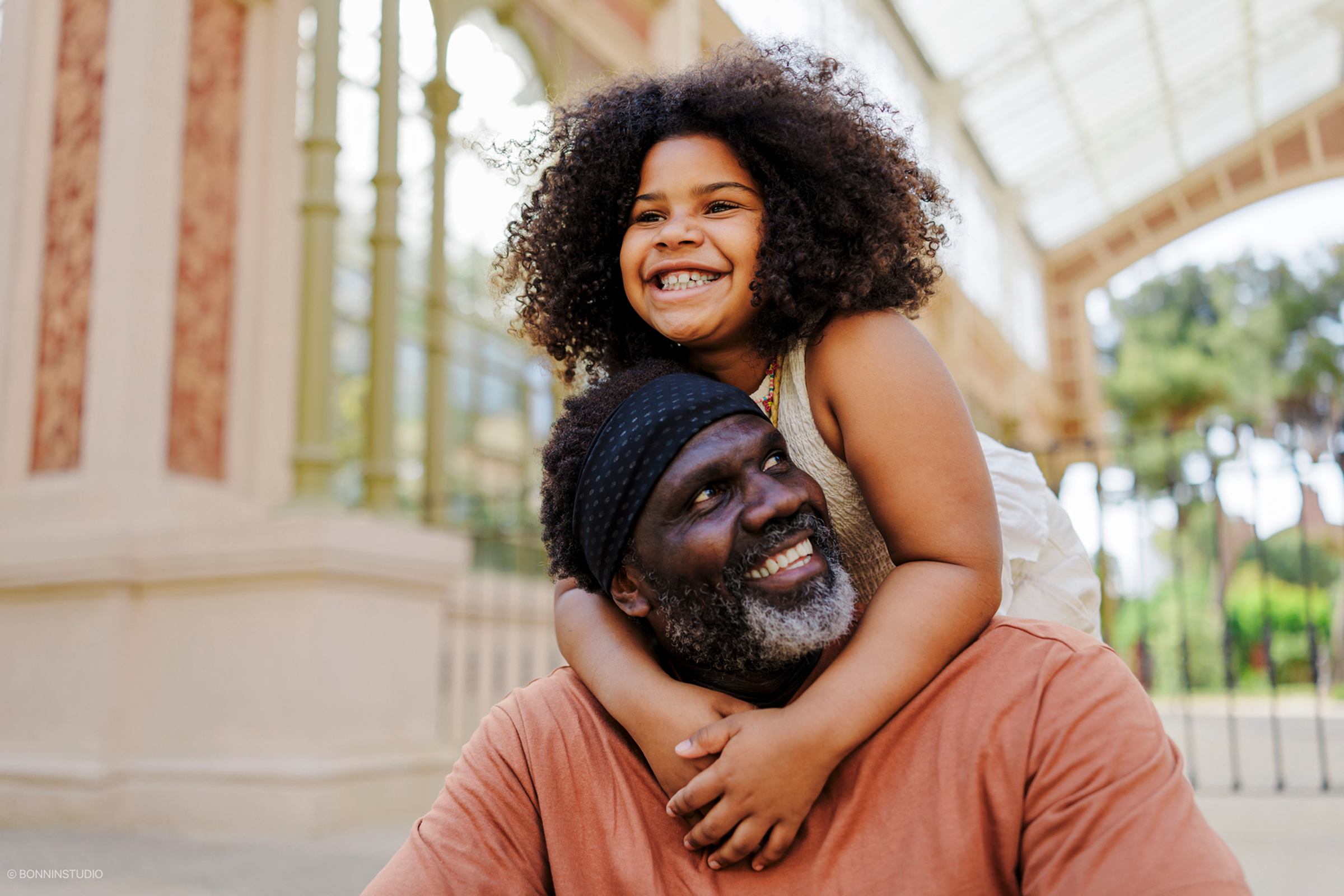 Smiling girl hugging an older man around the neck outdoors.