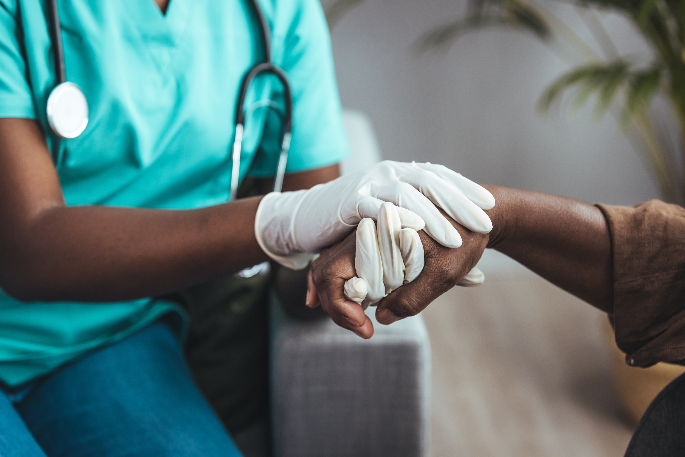 Healthcare provider in scrubs wearing gloves and holding a patient’s hand.