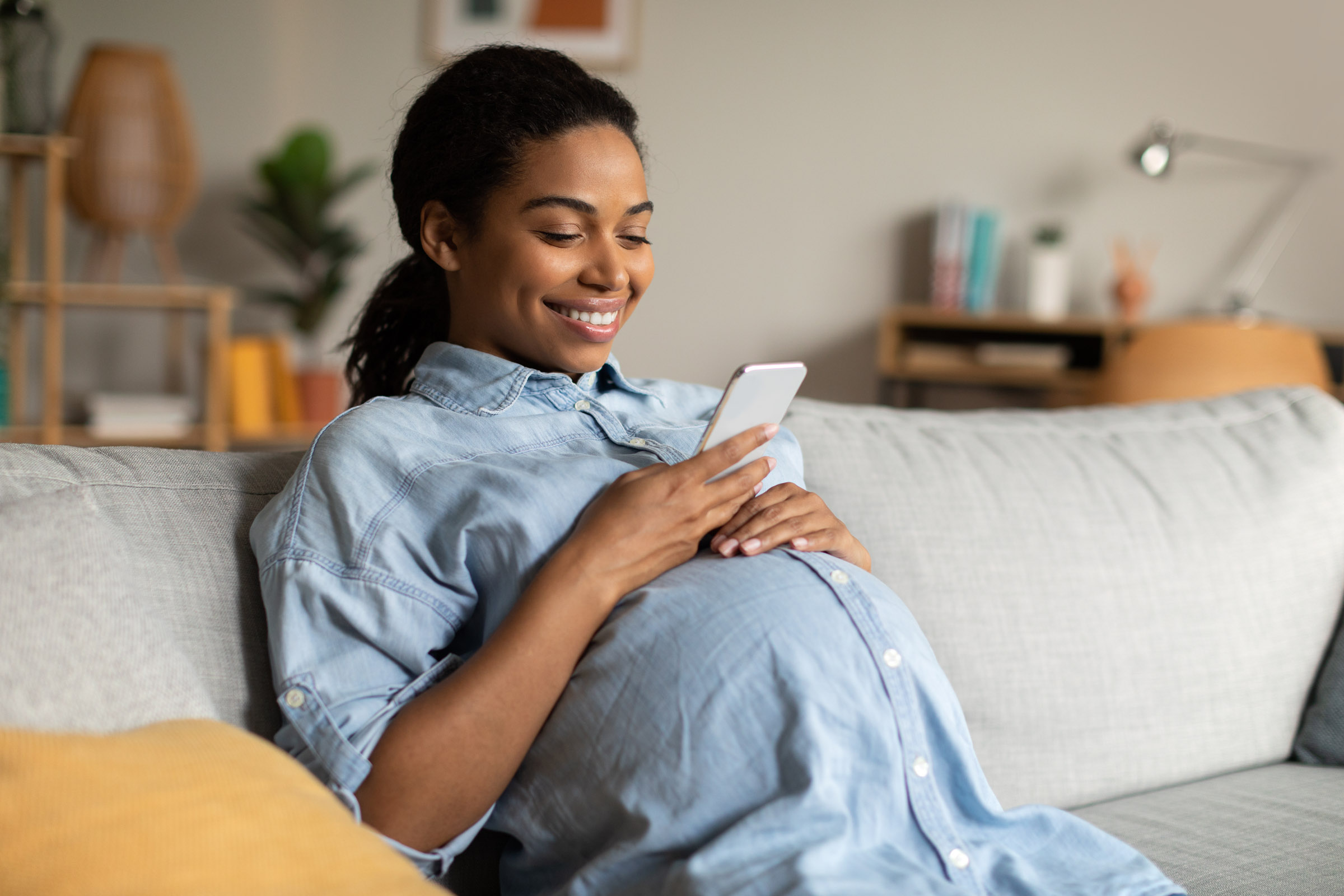 pregnant woman smiling at phone on couch