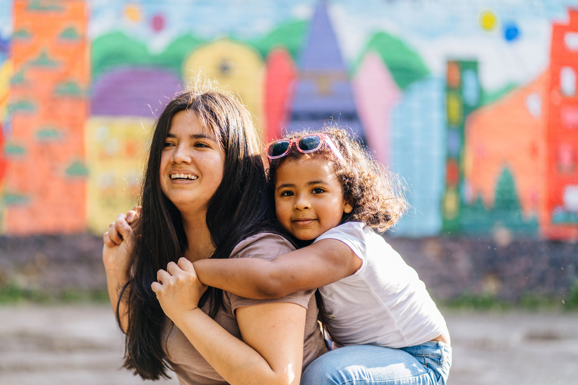 woman piggybacking girl in front of mural
